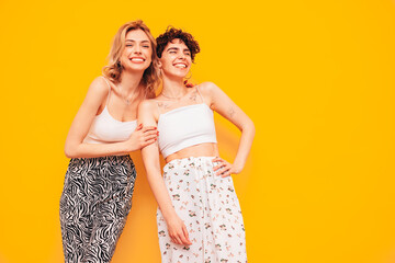Two young beautiful smiling brunette hipster female in trendy summer clothes. Sexy women posing near yellow wall in studio. Positive models having fun. Cheerful and happy