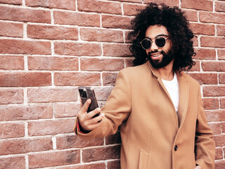 Handsome smiling hipster model.  Arabian man dressed in brown coat clothes. Fashion male posing in...
