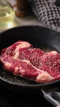 raw steak meat with pepper is cooking on a pan in heated oil, the process of cooking a steak