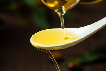 pouring olive oil in a wooden spoon on table.