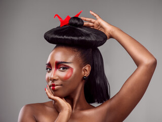 Portrait, makeup and black woman with origami in hair in studio isolated on gray background. Face,...