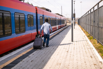 Man running to a leaving train along railway station with suitcase.	