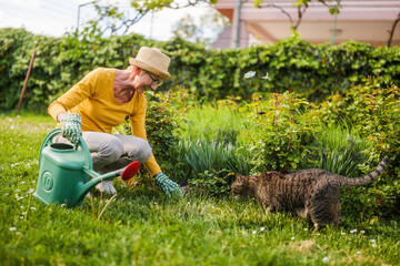 Senior woman enjoys gardening plants with her cute cat.	