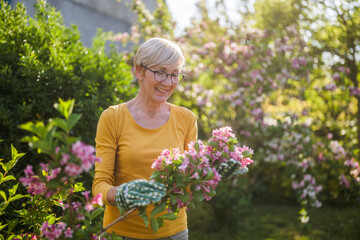 Happy senior woman enjoys looking at flowers in her garden.
