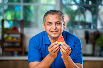 Indian asian man eating watermelon slice or tarbuj at home