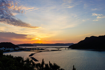 Naklejka premium 早暁の阿嘉島、天城（アマグスク）展望台。 東の座間味島から日が昇る。 右手から慶留間島、阿嘉大橋、阿嘉港が見える。 日本国沖縄県島尻郡慶良間諸島の阿嘉島にて。 2021年4月27日撮影。At Aka Island, Kerama Islands, Shimajiri-gun, Okinawa, Japan. Photographed on April 27, 2021. Amagusuku 