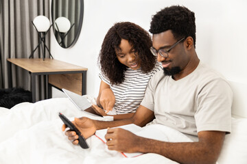 Couple Enjoying Leisure Time In Bedroom With Tablet And Book
