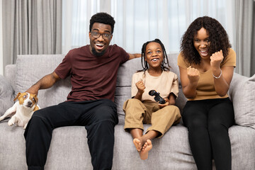 Happy Family Enjoying Video Game With Excited Child And Pet Dog On Couch At Home