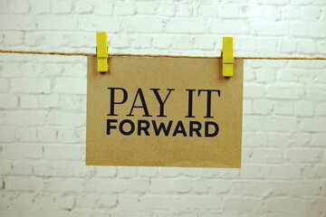 Pay it forward text on paper card hanging on the wall with Clothespins