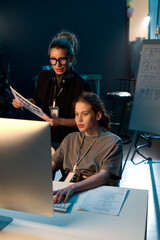 Vertical portrait of two women working in video production crew and using computer reviewing...