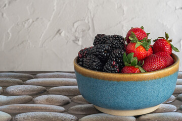 Bowl with strawberries and blackberries on a stone table. Seasonal fruits.
