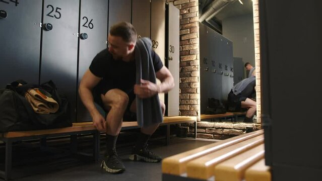 A dedicated athlete in a gym locker room attentively ties his shoelaces, reflecting the post-workout satisfaction of a rigorous training session, surrounded by the quiet atmosphere of the locker area.