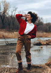 A girl in a red jacket and brown trousers against the background of a river

