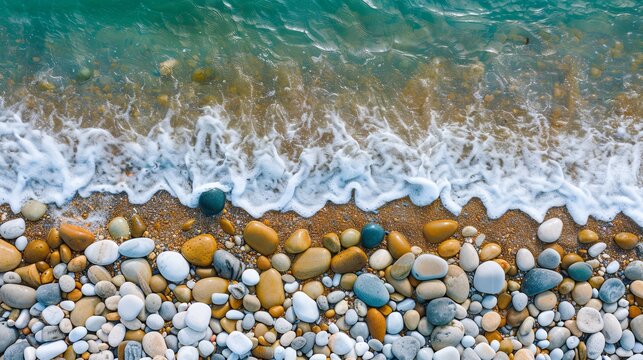 Tranquil shoreline featuring natural stone pebbles along the beach, gently caressed by the waves, captured from an aerial perspective using a drone camera.