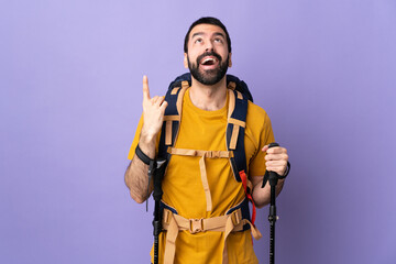 Caucasian handsome man with backpack and trekking poles over isolated background pointing up and surprised