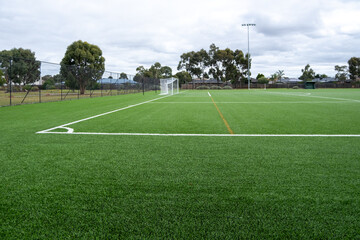 A large outdoor public soccer field with clean and new synthetic lawn or artificial grass covering the ground. Background texture of a sports park with a fake grass carpet. Copy space for design.