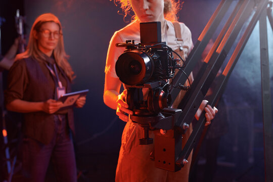Cropped shot of young woman operating video camera on rig in studio with neon lights copy space