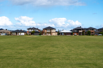 Background texture of a large vacant public sports ground with green grass lawn with some modern residential suburban houses in the distance. An outdoor park in Point Cook, Melbourne VIC Australia.