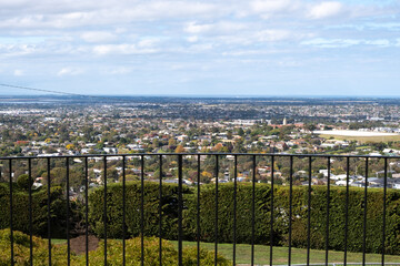 Elevated skyline view of Geelong's suburban neighborhood with many residential houses and Australian homes seen over a metal fence of a viewing platform at Wandana Heights Lookout, VIC, Australia.