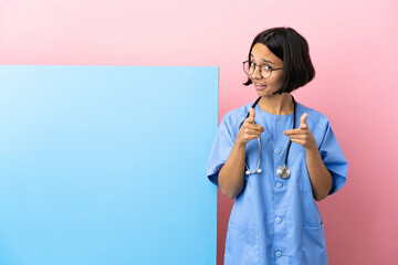 Young mixed race surgeon woman with a big banner over isolated background surprised and pointing...