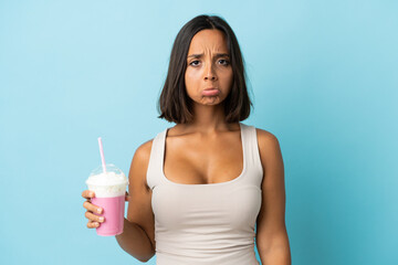 Young woman with strawberry milkshake isolated on blue background with sad expression