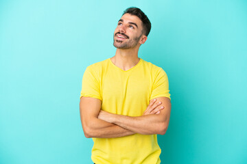 Young caucasian man isolated on blue background looking up while smiling
