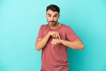 Young caucasian man isolated on blue background making the gesture of being late