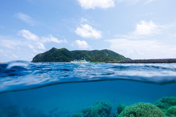 素晴らしいサンゴ礁の水面から見る、慶良間諸島フェリーのクイーンざまみ３世号と慶留間島の美しい半水面撮影。
圧倒的に大規模な素晴らしく美しいサンゴ礁。

沖縄県島尻郡座間味村阿嘉島の阿嘉ビーチにて。
2021年4月28日水中撮影。
A beautiful half-water shot of the Kerama Islands ferry Queen Zamami III and Geruma I