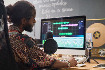 Focus on young Indian man looking at computer screen with frequency diagram of graphic audio...