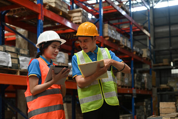 Manager and warehouse worker discussing controlling distribution and checking inventory in...