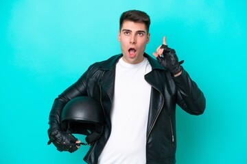 Young caucasian man with a motorcycle helmet isolated on blue background thinking an idea pointing...