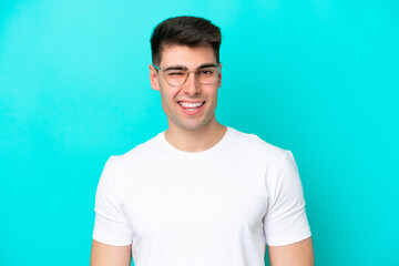 Young caucasian man isolated on blue background With glasses and happy expression