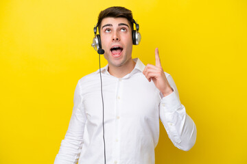 Telemarketer caucasian man working with a headset isolated on yellow background pointing up and...