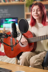 Focus on microphone fixed on desk in front of camera against talented teenage girl playing acoustic...