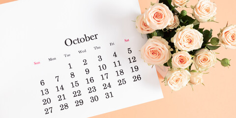 Fototapeta premium Flat desk paper calendar for October 2024, top view. Pale delicate roses on a beige background.