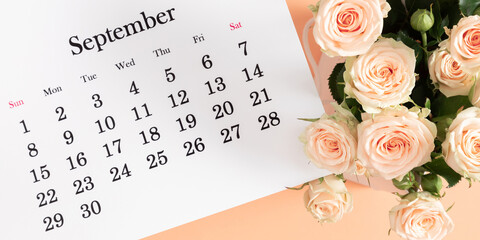 Fototapeta premium Flat desk paper calendar for September 2024, top view. Pale delicate roses on a beige background.