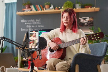 Cute teenage girl in casualwear sitting in armchair in front of microphone, performing new song and...