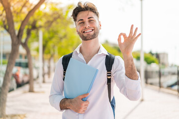 Young handsome student man at outdoors showing ok sign with fingers