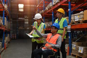 A senior warehouse supervisor with a disability in a wheelchair manages the work with the team,...
