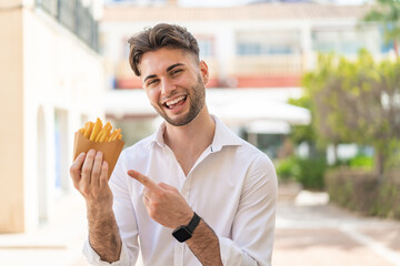 Young handsome man holding fried chips at outdoors and pointing it