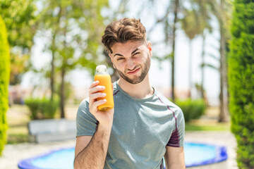 Young handsome sport man holding an orange juice at outdoors with sad expression