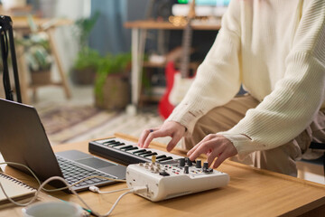 Hands of young woman turning consoles of sound mixing equipment and playing electric piano while...