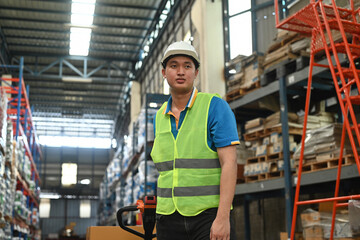 An Asian warehouse worker in a safety uniform pulling a load cart product to a shelf in a warehouse, Company employees arrange products. Warehouse industrial stock storage concept