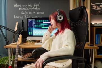 Side view of female teenager listening to new music in headphones while sitting in armchair by...