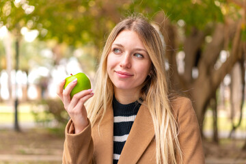 Young pretty blonde woman with an apple at outdoors