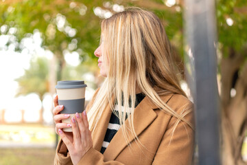 Young pretty blonde woman holding a take away coffee at outdoors in back position