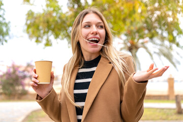 Young pretty blonde woman holding a take away coffee at outdoors with surprise facial expression