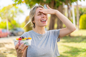 Young blonde woman holding a bowl of fruit at outdoors has realized something and intending the solution - obrazy, fototapety, plakaty