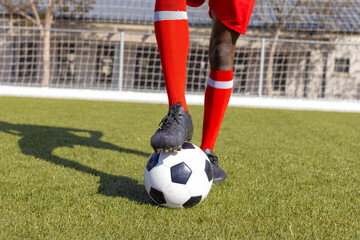 African American youth in red socks, cleats steps on soccer ball outside