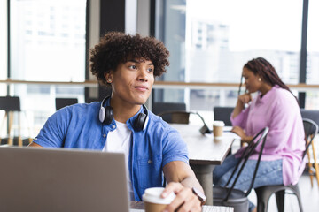 Biracial man with curly hair uses laptop in office, woman in background - Powered by Adobe